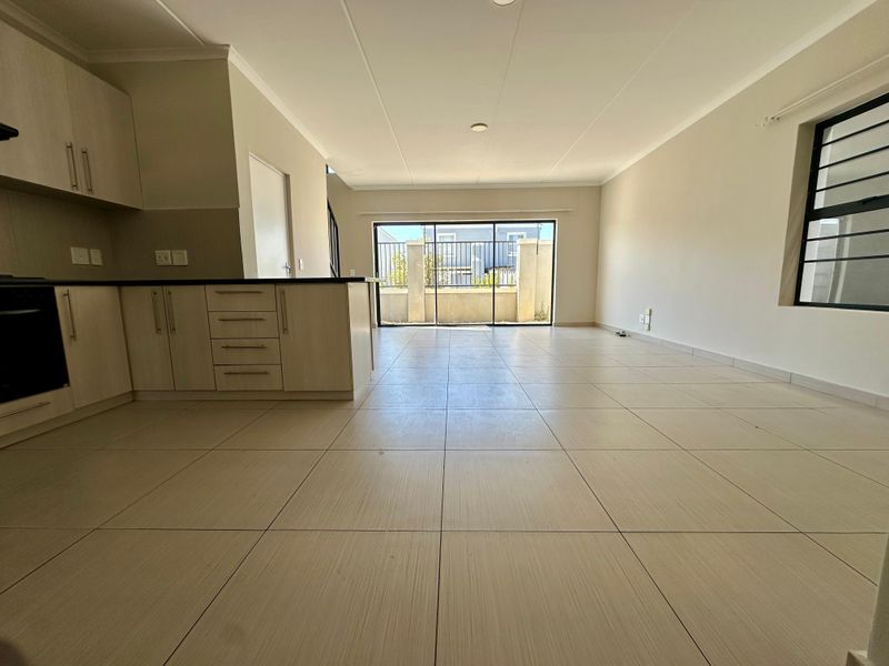 Spacious open-plan living area featuring a modern kitchen with built-in cabinetry and tiled flooring, leading out to a private patio through sliding glass doors.