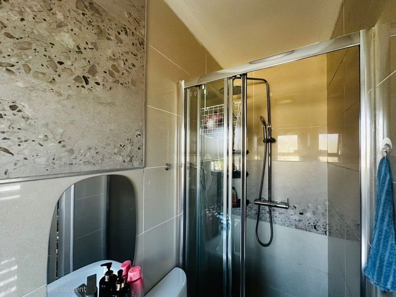 A modern bathroom featuring a glass shower enclosure, contemporary terrazzo-style wall tiling, and a vanity mirror.