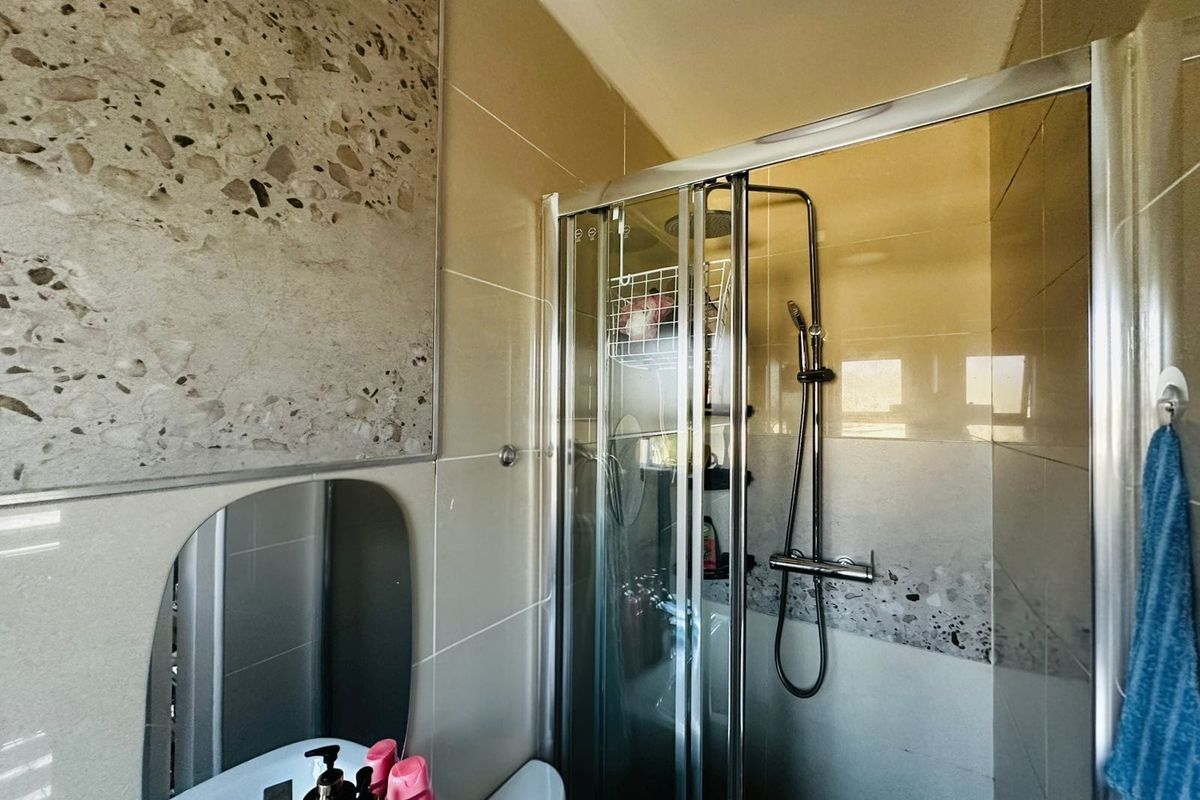 A modern bathroom featuring a glass shower enclosure, contemporary terrazzo-style wall tiling, and a vanity mirror.