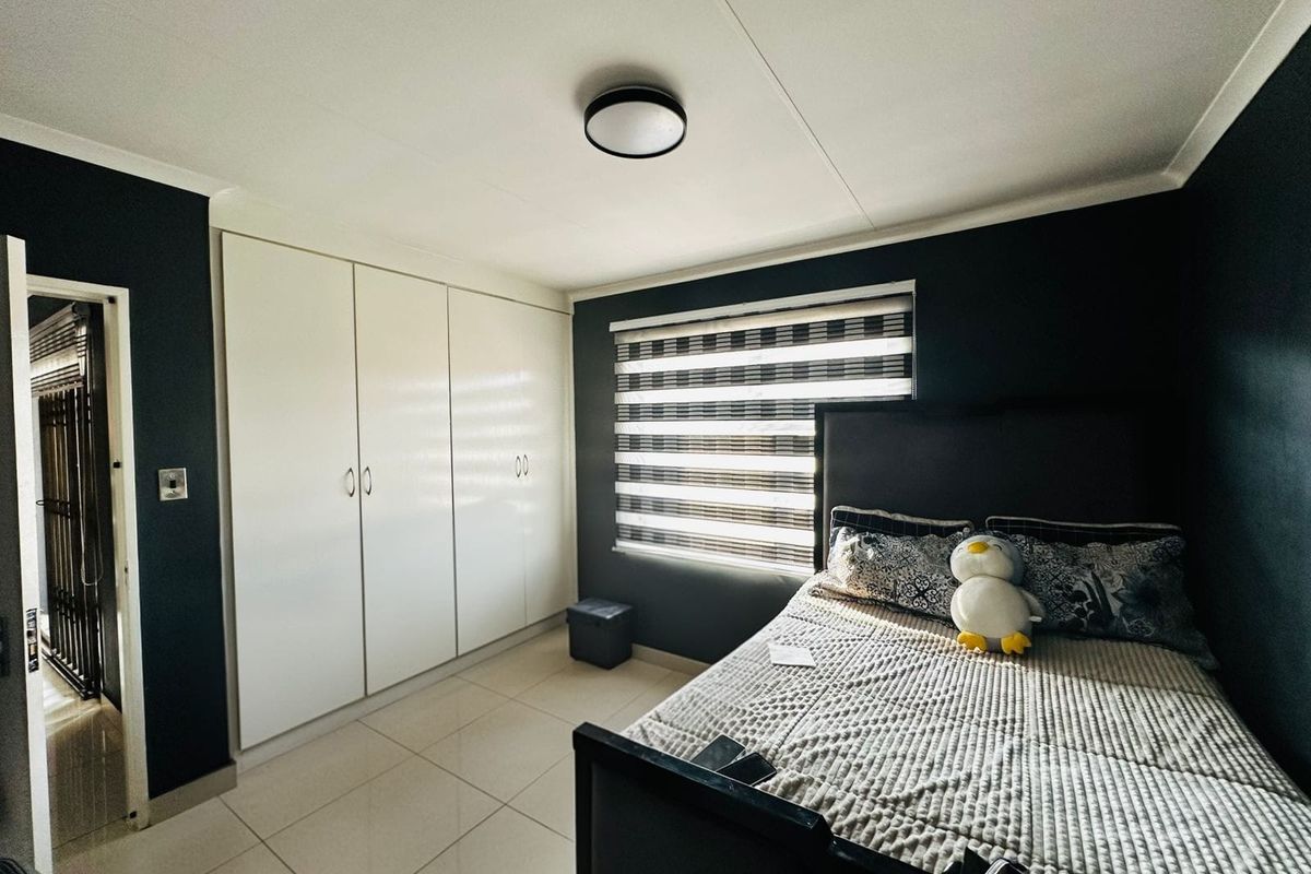 A well-maintained bedroom featuring built-in cupboards, tiled flooring, and modern roller blinds, offering a clean and functional living space.