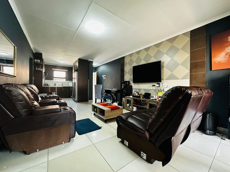 Open-plan living area featuring tiled floors, a feature wall with mounted television, and an integrated kitchen space with built-in cabinetry.