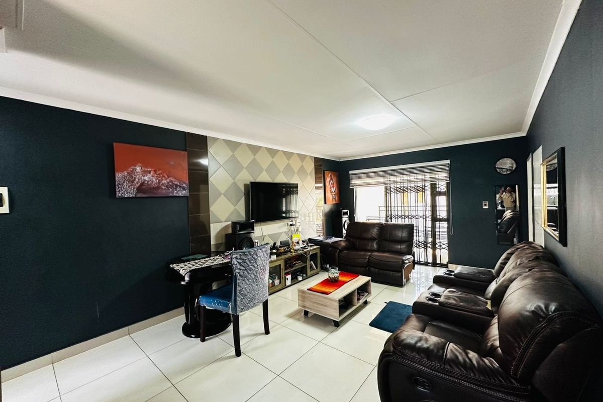 A living room featuring tiled flooring, a decorative tiled feature wall, and access to an outdoor area through a security gate.