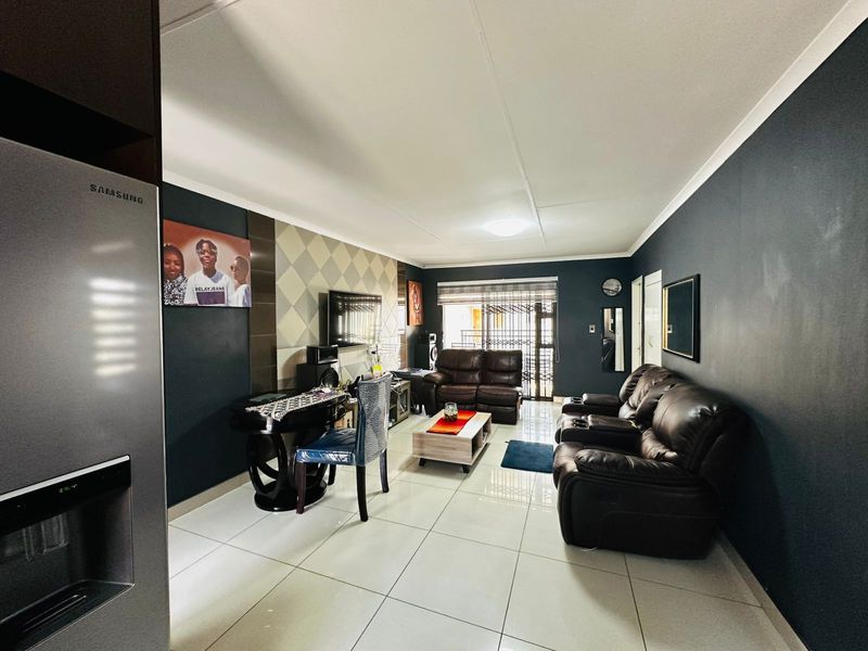 A well-maintained living room featuring large format floor tiles, a decorative feature wall, and access to an outdoor area through a security gate.