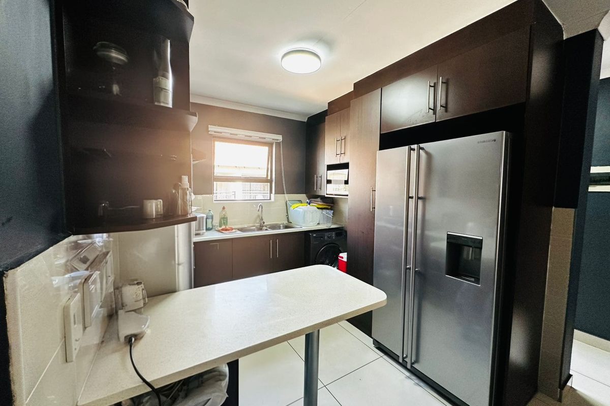 A functional kitchen featuring dark wood cabinetry, a breakfast counter, tiled flooring, and space for a large refrigerator.