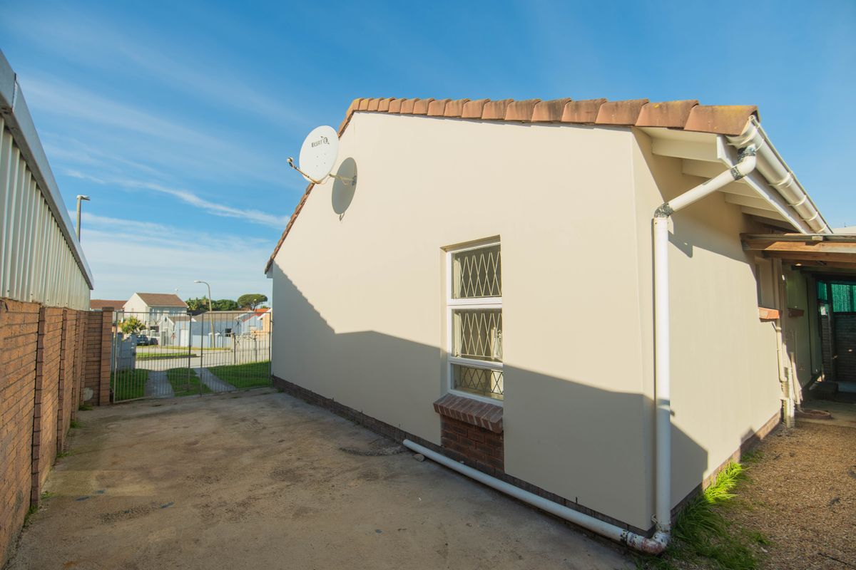 Side view of the property showing the exterior wall, security window bars, satellite dish, and concrete paving area.