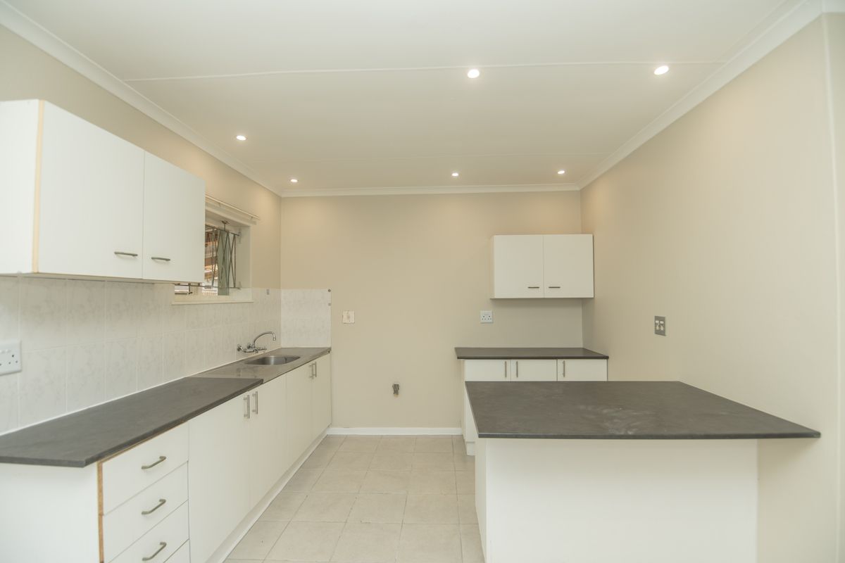 A clean, functional kitchen featuring white cabinetry, dark laminate countertops, tiled backsplash, and recessed lighting in an open, neutral-toned space.