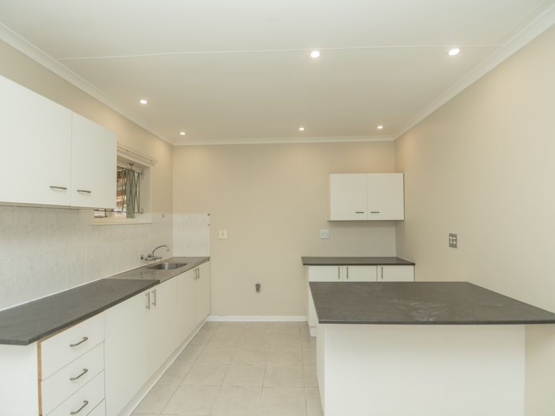A clean, functional kitchen featuring white cabinetry, dark laminate countertops, tiled backsplash, and recessed lighting in an open, neutral-toned space.
