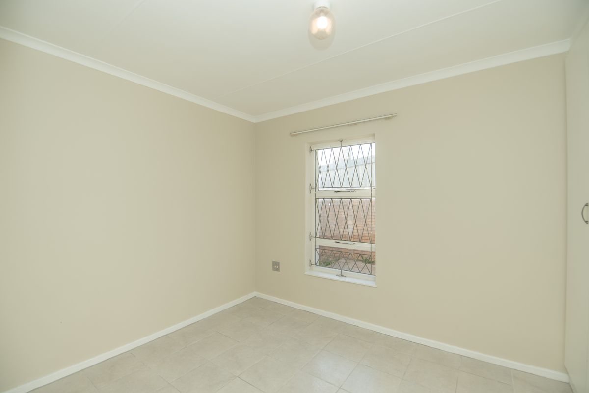 A clean, empty bedroom featuring neutral walls, tiled flooring, and a built-in wardrobe with security bars on the window.