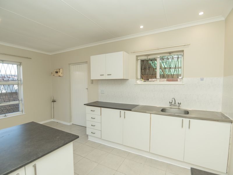 A functional, empty kitchen featuring white cabinetry, stainless steel sink, laminate countertops, and tiled flooring, ready for a modern update.