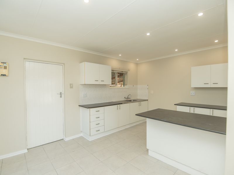 A clean, functional kitchen featuring white cabinetry, dark laminate countertops, a stainless steel sink, and neutral tiled flooring with recessed lighting.