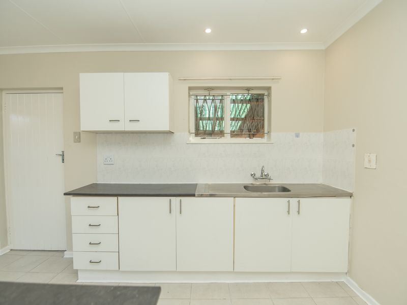 A functional kitchen featuring white built-in cabinetry, a stainless steel sink, tiled splashback, and recessed lighting, offering a clean and practical workspace.