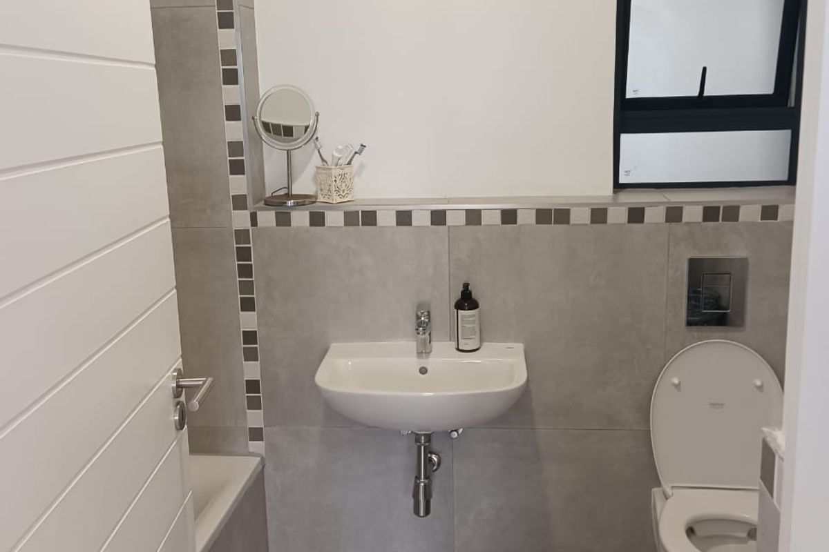 A modern, well-maintained bathroom featuring a wall-mounted basin, wall-hung toilet with concealed cistern, and neutral grey tiling.
