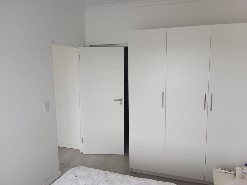 A clean bedroom featuring modern white built-in cupboards and neutral tiled flooring, providing ample storage and a bright, minimalist aesthetic.