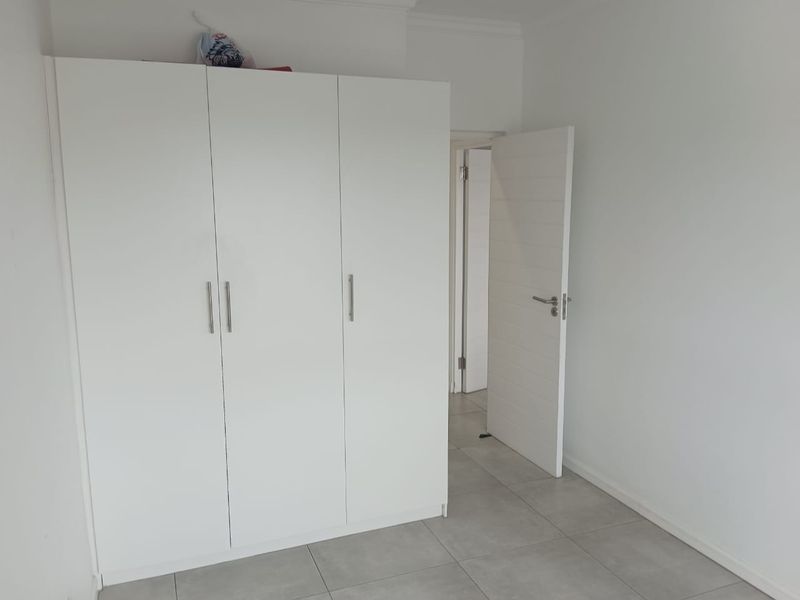 A clean, minimalist bedroom featuring neutral tiled flooring and a large white built-in wardrobe.