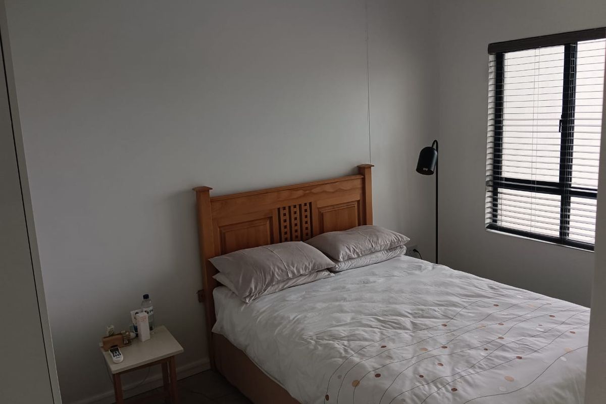 A functional bedroom featuring a window with venetian blinds and a built-in wardrobe, offering a neutral space ready for personalization.
