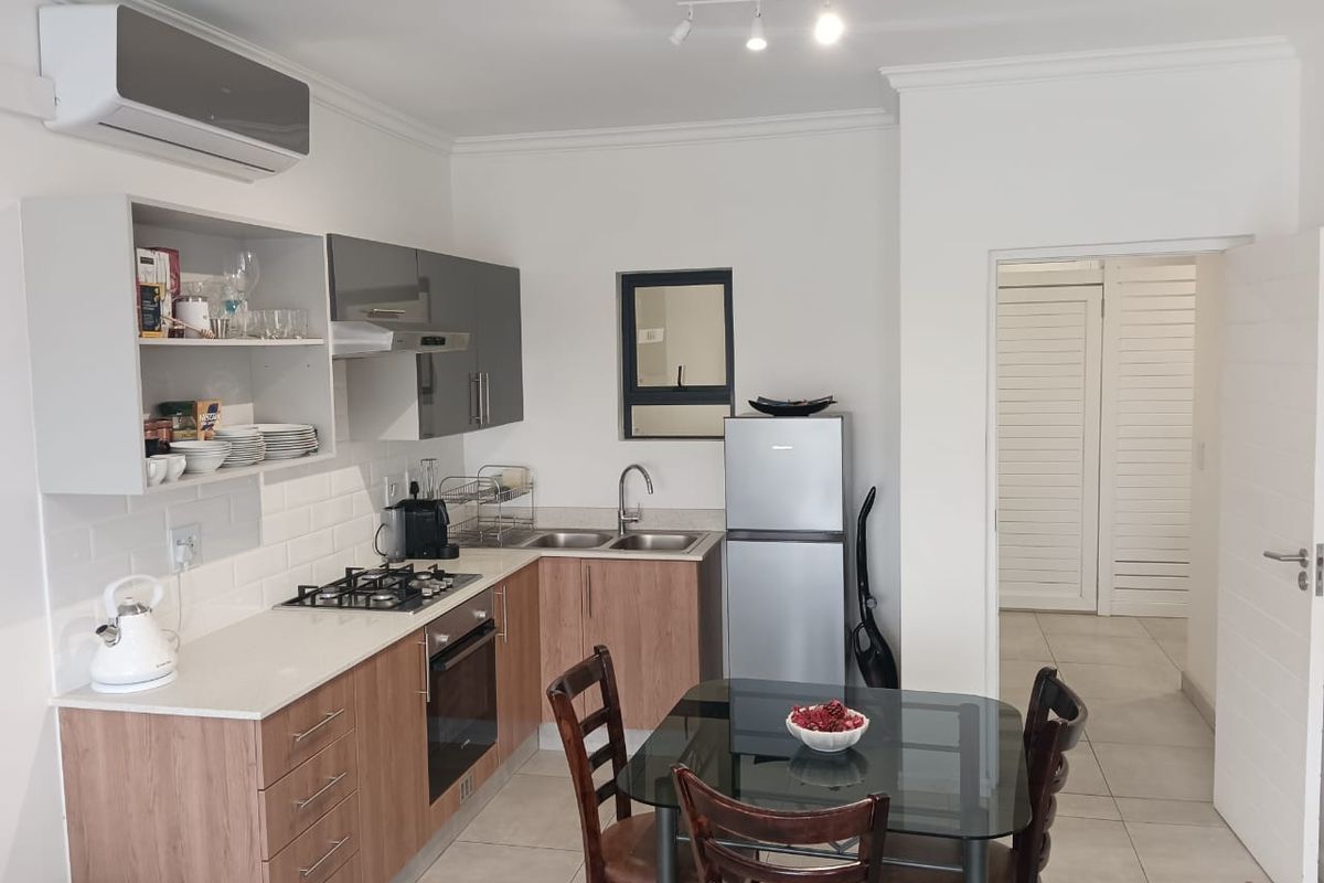 Modern open-plan kitchen featuring wood-finish cabinetry, quartz countertops, gas hob, built-in oven, and air conditioning, seamlessly flowing into the dining area.