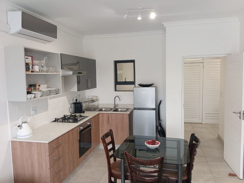 Modern open-plan kitchen featuring wood-finish cabinetry, quartz countertops, gas hob, built-in oven, and air conditioning, seamlessly flowing into the dining area.