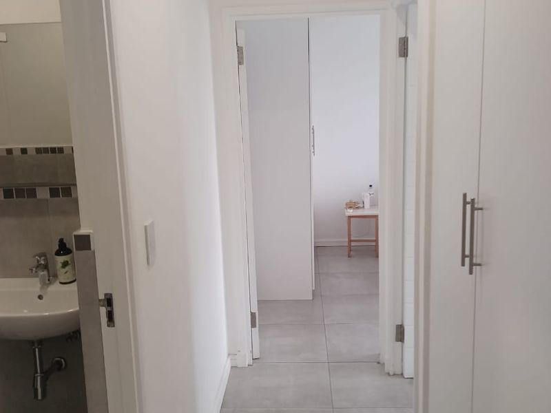 A clean, neutral hallway featuring tiled flooring and built-in storage cupboards, providing access to adjacent rooms including a bathroom.