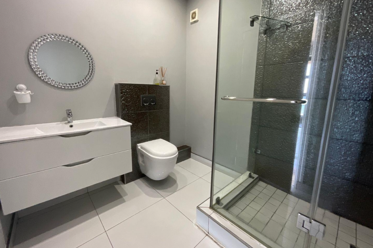 Modern bathroom featuring a wall-mounted vanity, wall-hung toilet with concealed cistern, and a glass-enclosed shower with mosaic tile accents.