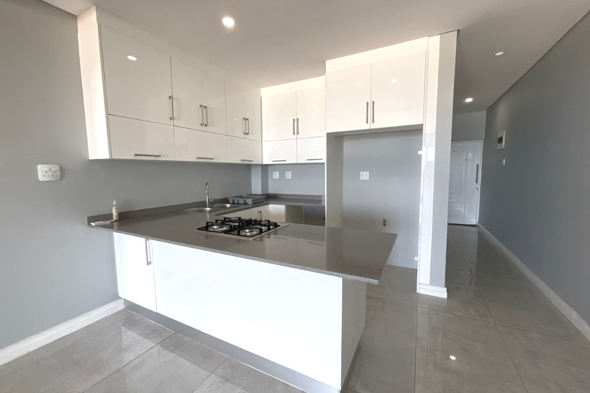 Modern kitchen featuring white high-gloss cabinetry, stone countertops, a built-in gas hob, and sleek tiled flooring in an open-plan layout.