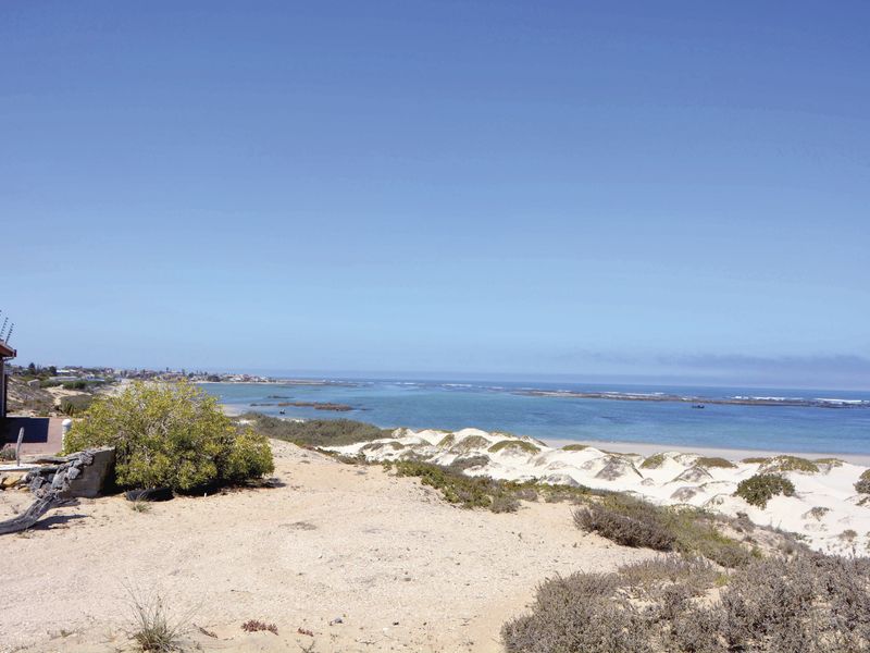 A scenic elevated view overlooking the coastline, featuring pristine sand dunes and clear blue ocean waters.