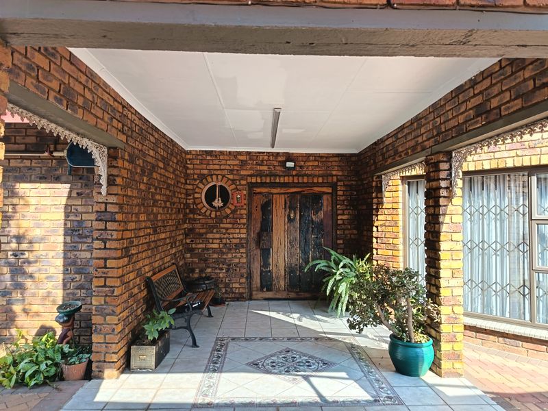 Covered entrance porch featuring exposed brickwork, decorative tiled flooring, and a rustic timber front door.