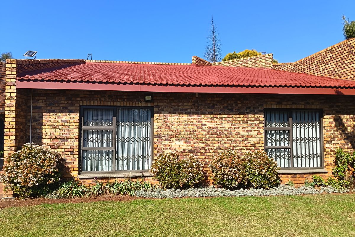 Rear view of a face brick house featuring a tiled roof, aluminium window frames with security gates, and a well-maintained garden.