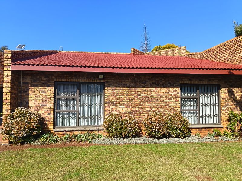 Rear view of a face brick house featuring a tiled roof, aluminium window frames with security gates, and a well-maintained garden.