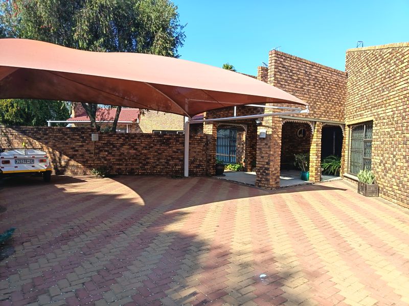 A well-maintained face brick house exterior featuring a paved driveway, a large shade sail carport, and secure entrance access.