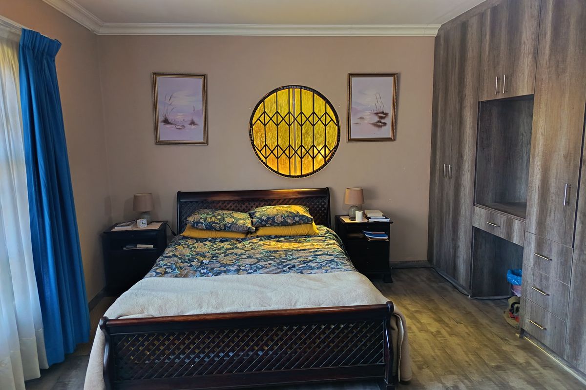 A well-maintained bedroom featuring built-in wooden cupboards, laminate flooring, and a unique circular decorative window.