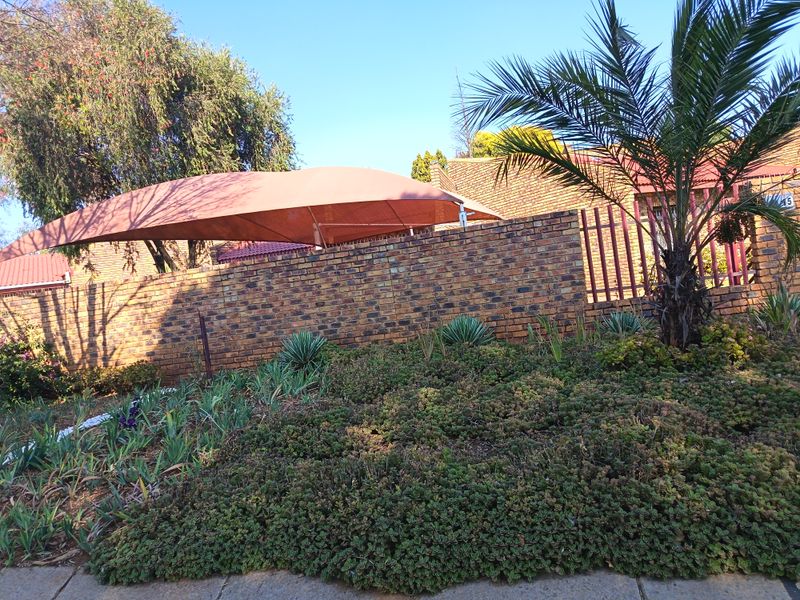 Front exterior view featuring a brick boundary wall, established garden landscaping, and a large shade sail structure.