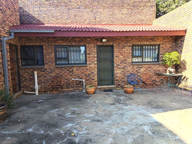 Rear exterior view of a face brick house featuring a covered patio area with concrete paving and secure window and door access.