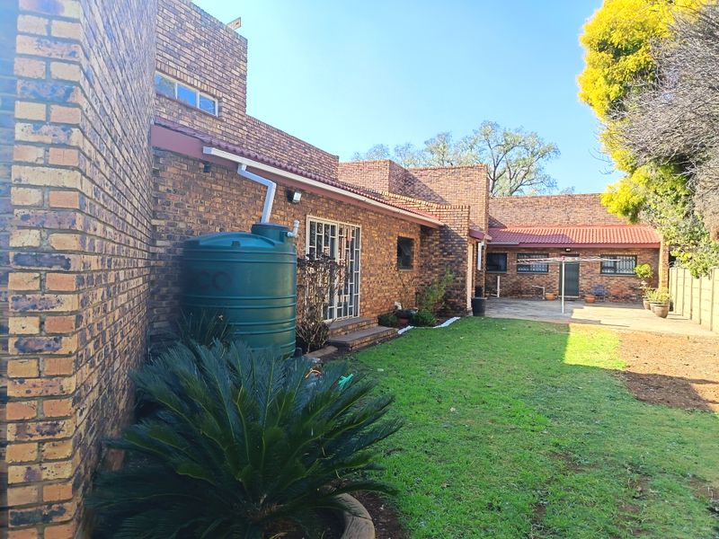 Rear view of the property featuring a face brick facade, a lawned garden, a paved patio area, and an installed water storage tank.