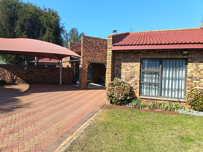 Front view of a face brick house featuring a paved driveway, shade sail carport, tiled roof, and secure window treatments.