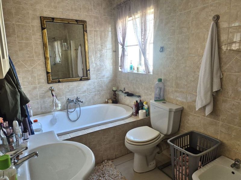 A functional bathroom featuring a built-in bathtub, pedestal washbasin, bidet, and toilet, finished with neutral ceramic wall tiling.