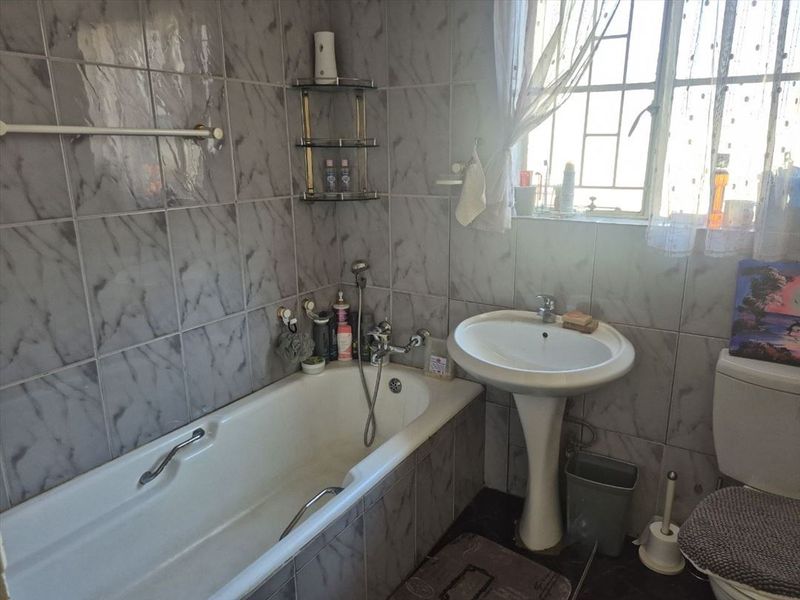 A functional bathroom featuring a pedestal basin, bathtub with handheld shower, and full-height marble-effect wall tiling.
