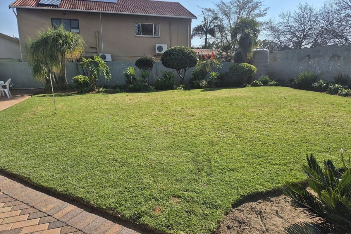 Spacious rear garden featuring a well-maintained lawn, paved area, boundary wall, and exterior building infrastructure including solar panels and air conditioning units.