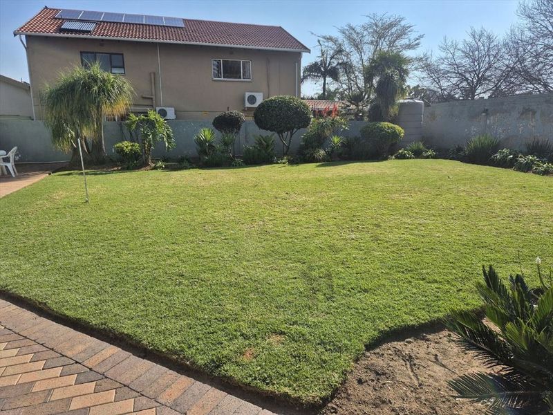 Spacious rear garden featuring a well-maintained lawn, paved area, boundary wall, and exterior building infrastructure including solar panels and air conditioning units.