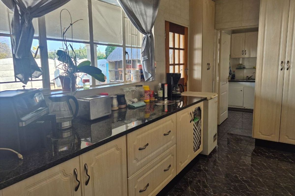 A functional kitchen featuring granite countertops, ample built-in cabinetry, and tiled flooring, with a view through the window to the exterior.