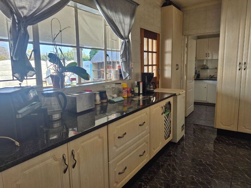 A functional kitchen featuring granite countertops, ample built-in cabinetry, and tiled flooring, with a view through the window to the exterior.