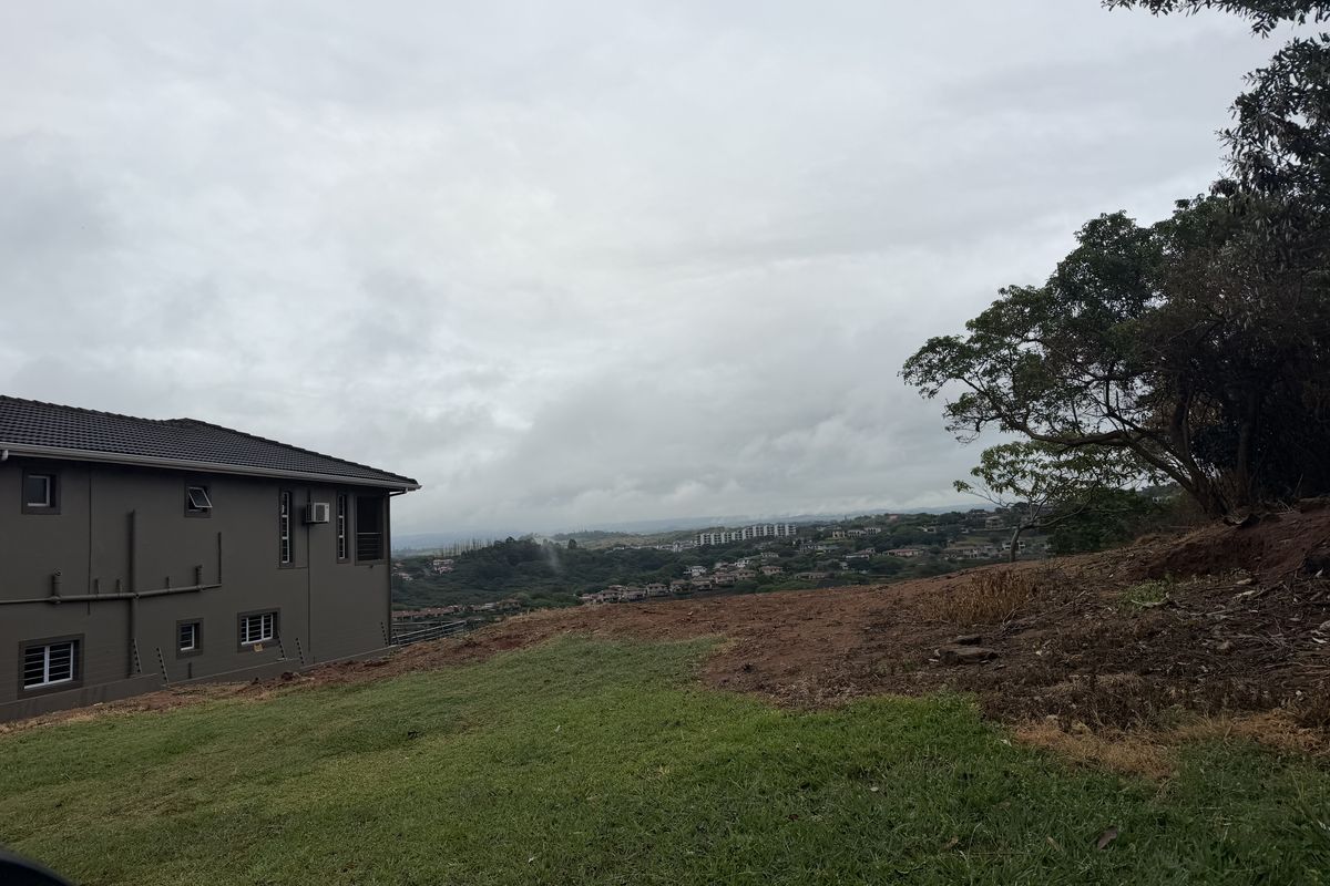 A view of the sloped residential land parcel with an adjacent property and distant landscape scenery.