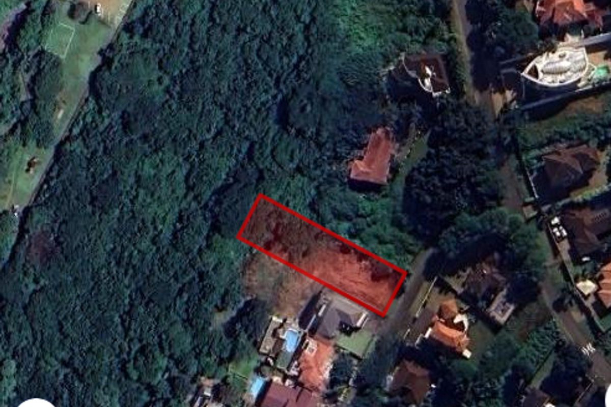 Aerial view of a vacant residential plot highlighted in red, situated within a developed suburban neighborhood surrounded by dense vegetation.