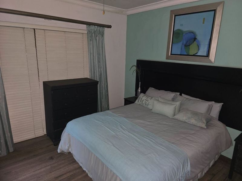 A bedroom featuring laminate flooring, a sliding door with blinds, and a feature wall.