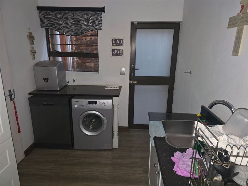 A functional laundry area featuring dark stone countertops, a stainless steel sink, and direct access to the exterior via a frosted glass door.