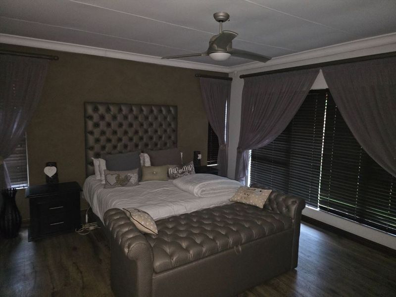 A well-maintained bedroom featuring laminate flooring, a ceiling fan, and dark venetian blinds, creating a cozy and private atmosphere.