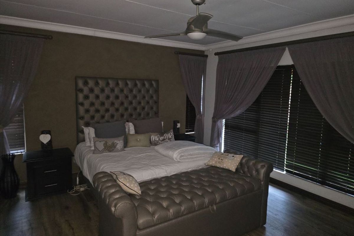 A well-maintained bedroom featuring laminate flooring, a ceiling fan, and dark venetian blinds, creating a cozy and private atmosphere.