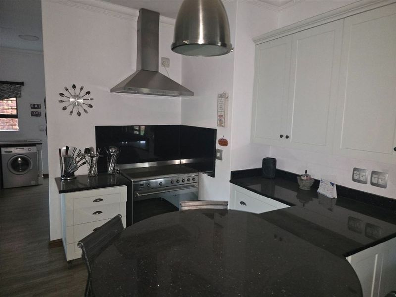 A functional kitchen featuring white cabinetry, dark granite countertops, a stainless steel extractor fan, and a glass splashback.