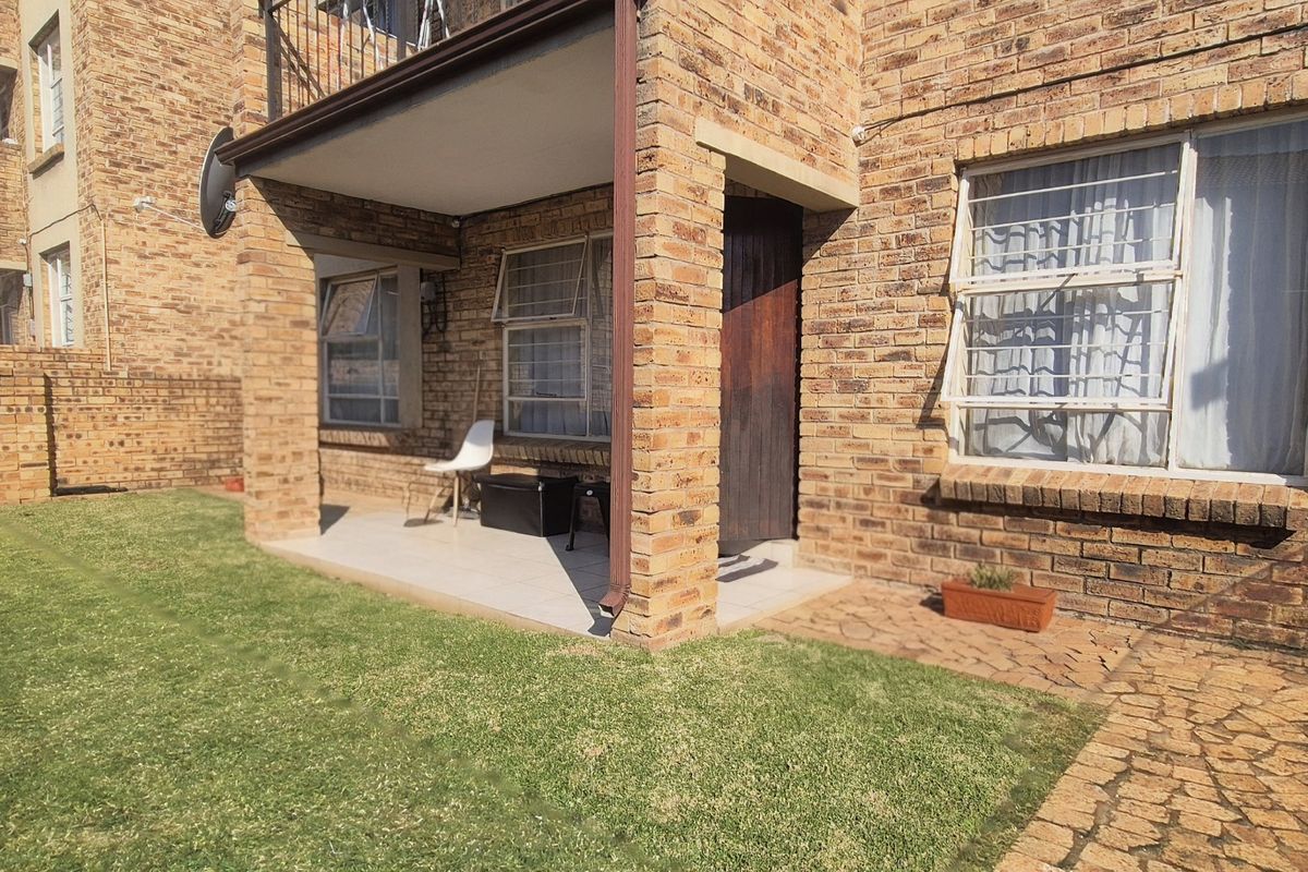 Rear view of a face brick apartment unit featuring a covered patio, paved walkway, and private garden area.