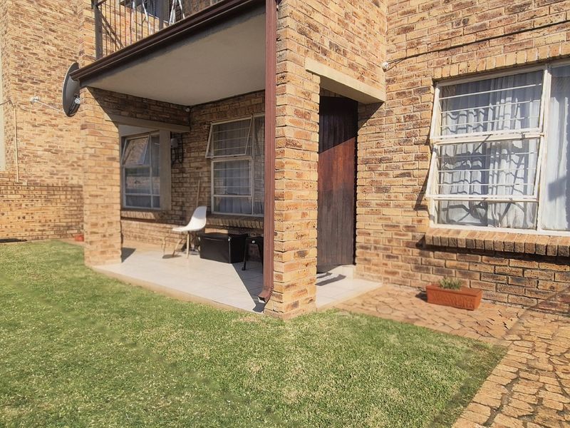 Rear view of a face brick apartment unit featuring a covered patio, paved walkway, and private garden area.