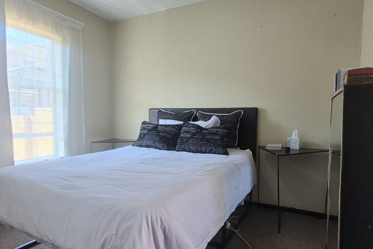 A standard bedroom featuring carpeted flooring and natural light from a window with installed curtain tracks.